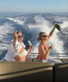 two women sitting on the back of a boat drinking wine and holding up champagne flutes