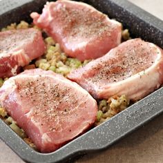 three raw pork chops in a pan with rice and seasoning sprinkled on top