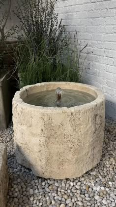 there is a stone water fountain in the middle of some rocks and gravel next to a brick wall