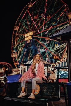 a woman sitting on top of a bench in front of a ferris wheel at night