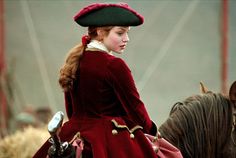 a woman in red riding on the back of a black horse wearing a hat and coat