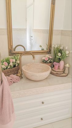 a bathroom sink sitting under a large mirror next to a wooden basket filled with flowers