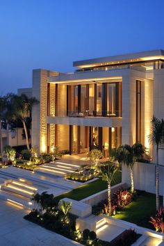 a modern house with lots of plants and lights on the front yard at night time