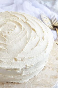 a white frosted cake sitting on top of a plate next to a knife and fork