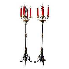 two tall red candles are standing next to each other on black iron stands with gold trimmings