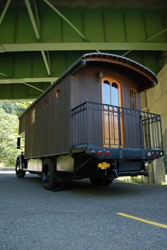 a truck is parked under a bridge with a small house on the back and balcony