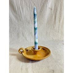 a small candle is sitting in a gold dish on a white background with a blue and green stripe