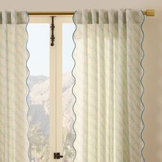 an open window with white curtains and blue scalloped trim on the top, in front of a mountain view