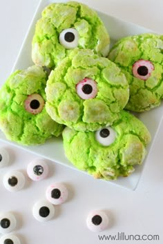 green monster cookies with googly eyes are on a white platter next to eyeballs