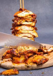 a stack of chicken skewers on top of a cutting board next to a knife