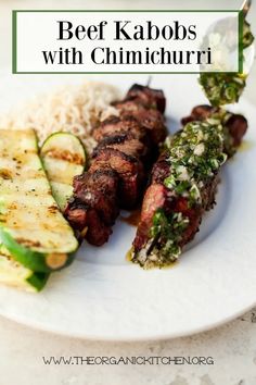 a white plate topped with meat and veggies on skewers next to rice