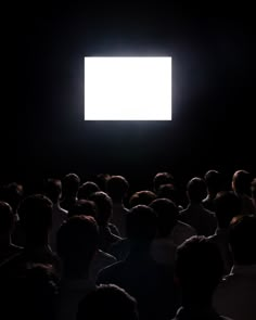 a large group of people sitting in front of a white light on a black background