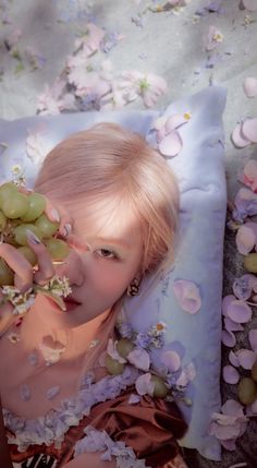 a woman laying on top of a bed covered in flowers next to a bunch of grapes