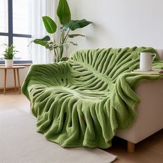 a living room with a couch covered in a green blanket next to a potted plant