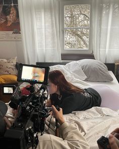 a woman laying on top of a bed next to a camera set up in front of a window