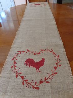 a table runner with a rooster in a heart design on it, sitting on top of a wooden table