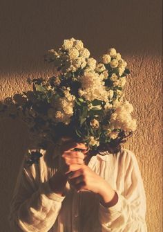 a person with flowers on their head is holding something in front of his face while standing against a wall