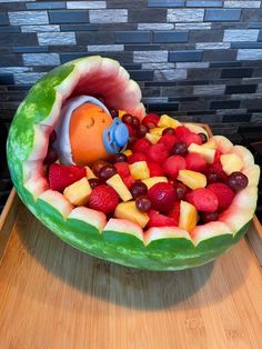 a watermelon bowl filled with fruit and an orange fish in it's mouth