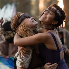 two young women hugging each other in front of a group of people at an outdoor event