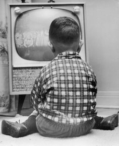 a young boy sitting on the floor in front of an old tv watching television with his legs crossed