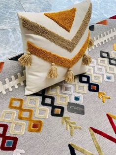 a decorative pillow with tassels on it sitting on top of a colorful rug