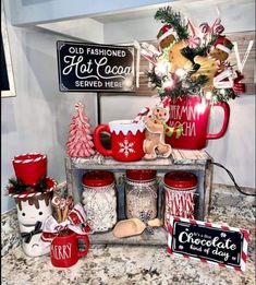 red mugs filled with candy and christmas decorations on top of a counter next to signs