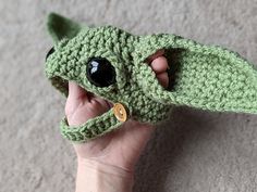 a crocheted baby yoda hat is held up by someone's hand