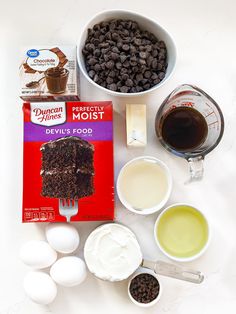 ingredients to make chocolate cake laid out on a white counter top, including eggs, milk, flour, butter, and chocolate chips