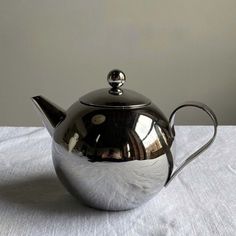 a silver teapot sitting on top of a white table cloth with a metal handle