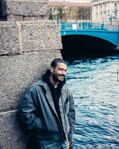 a man leaning against the side of a stone wall next to a body of water