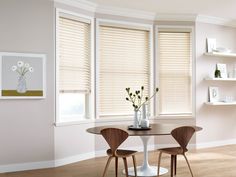 a dining room table with two chairs and vases on top of it in front of three windows