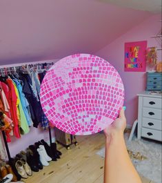 a person holding up a pink paper plate in front of a rack of clothes and shoes