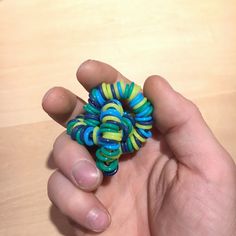 a hand holding a small colorful bead in it's left hand on a wooden surface