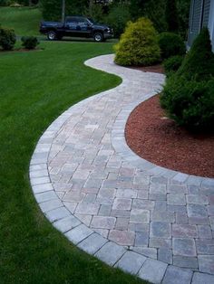 a brick walkway in front of a house with cars parked on the driveway and green grass