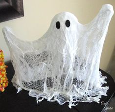 two white plastic ghost statues sitting on top of a black table next to candy corn