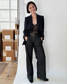 a woman standing in front of a white wall wearing black pants and a blazer