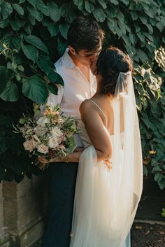 a bride and groom standing next to each other in front of a bush with greenery