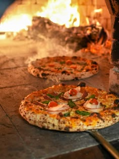 two pizzas sitting on top of a table next to a fire