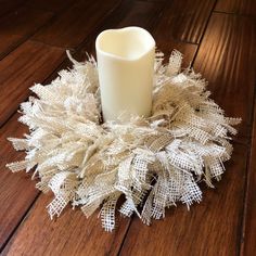 a white candle sitting on top of a wooden floor next to a wreath covered in burlap