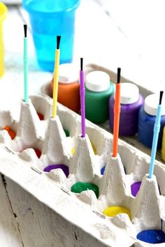 an egg carton filled with different colored eggs next to markers and paint tubes on top of it