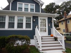 a blue house with white trim and stairs leading up to the front door, on a cloudy day