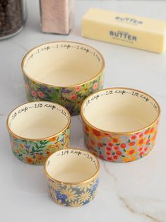 four flowered bowls sitting on top of a white counter next to some chocolates