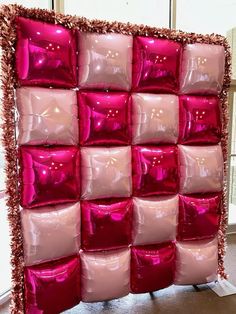 pink and red pillows are arranged in a square pattern on the wall, with gold fringes around them