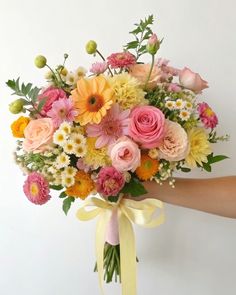 a bouquet of flowers is being held by a person's hand with a yellow ribbon