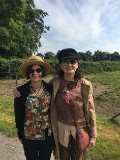 two women standing next to each other on a dirt road wearing hats and sun glasses