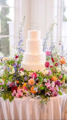 a white wedding cake sitting on top of a table covered in flowers and greenery