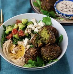 a bowl filled with meatballs and vegetables on top of a blue table cloth next to silverware