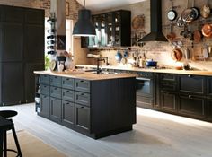 a large kitchen with black cabinets and wooden counter tops, along with hanging pots and pans on the wall