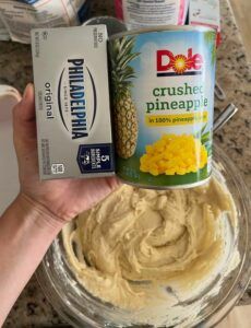 a hand holding a can of pineapple hump next to a container of dip