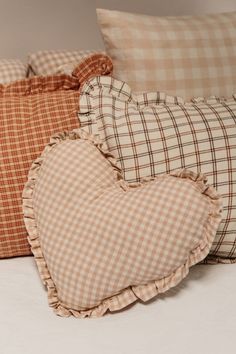 three pillows with ruffles on them are sitting on a bed, one in the shape of a heart